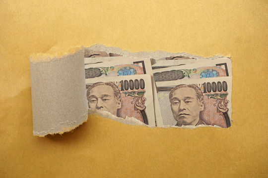 破れた紙の向こう側に覗く複数の一万円札