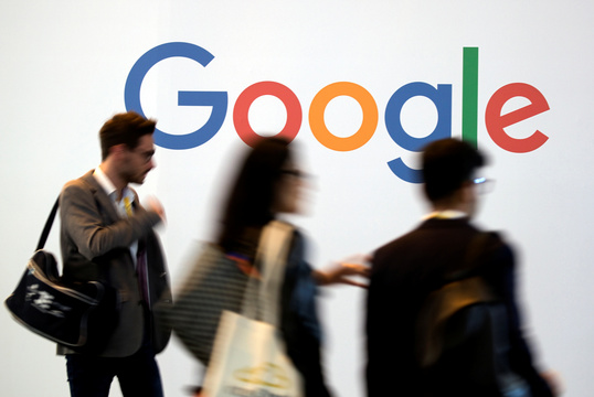 Googleロゴの前を通り過ぎる人々。