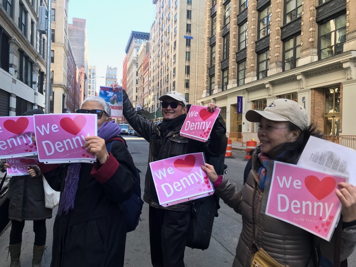 ｢ウィー・ラブ・デニー｣と書いた紙で玉城知事を歓迎する沖縄ゆかりの市民たち。