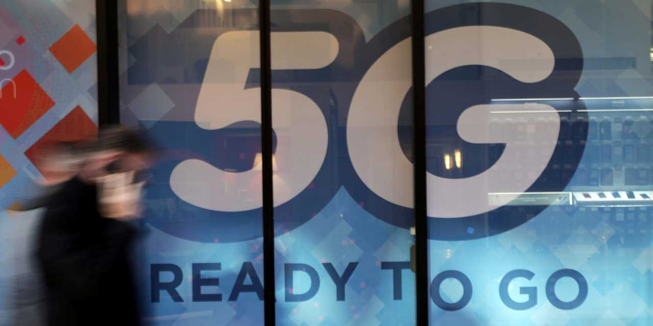 5Gのサインの前を歩く人。