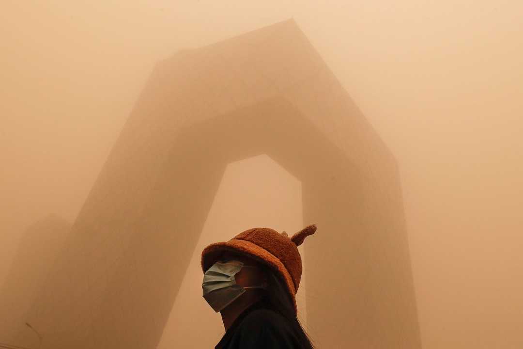 中国中央電視台（CCTV）の建物の前に立つフェイスマスクを着用した女性。2021年3月15日、北京は汚染された空気と砂嵐に見舞われた。