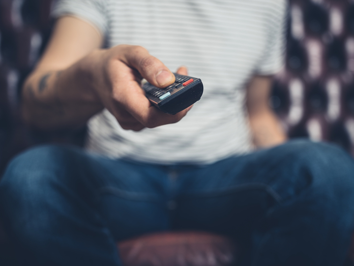 男性がテレビのリモコンを触っているイメージ写真