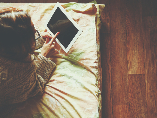 ベッドの上でタブレットをさわる女性