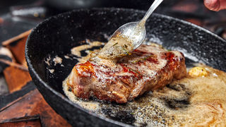 フライパンで焼けた肉にバターソースをかけている