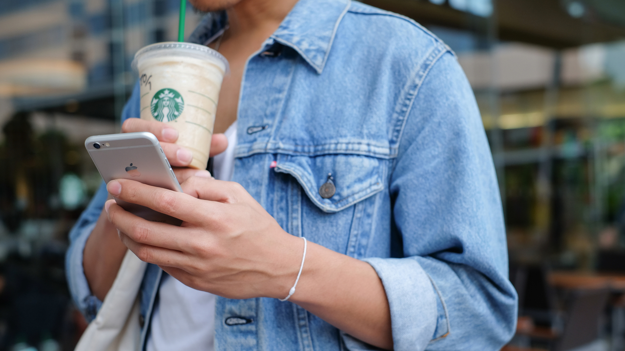 スタバのドリンクを飲みながらスマホを使う女性