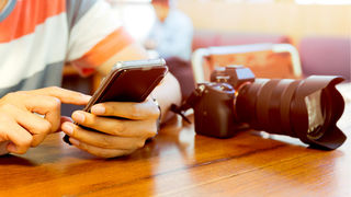 デジタル一眼レフカメラを横に置いて、スマホをいじっている人