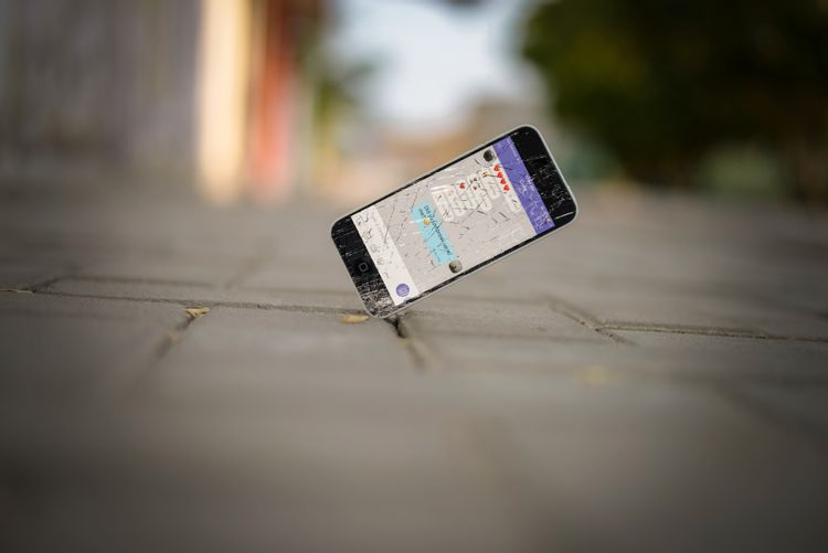 路上に立っている画面がひび割れたスマホ
