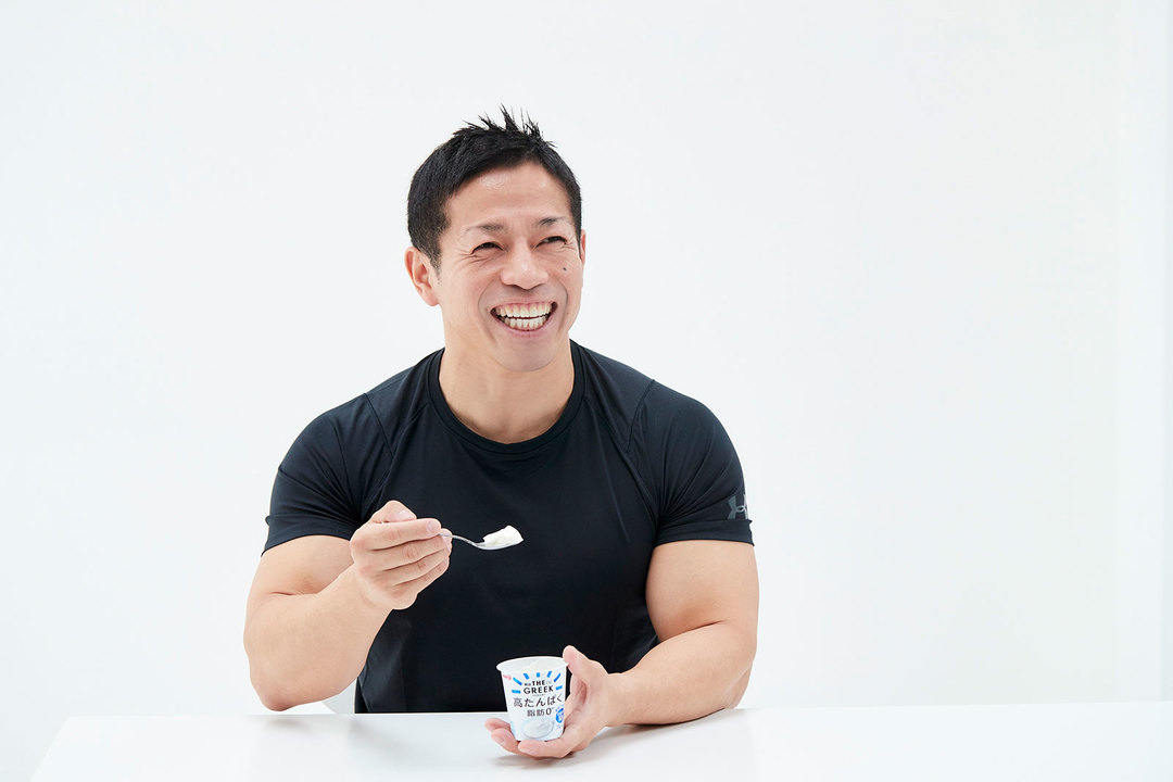 《明治THE GREEK YOGURT》を口にして思わず笑みがこぼれる岡田先生。「こんなに美味しくて高タンパクなヨーグルトがコンビニで買えるって、凄い時代ですよ!」